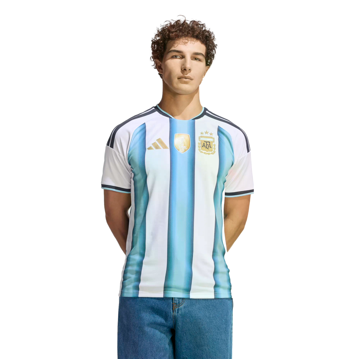 A man with curly hair wearing a blue and white striped Argentina national football team jersey and jeans, standing against a black background.