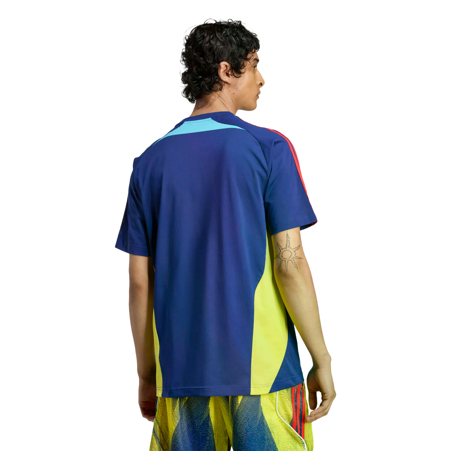 Back view of a man wearing a blue sports shirt with yellow side panels and red shoulder stripes, paired with yellow patterned shorts against a black background.