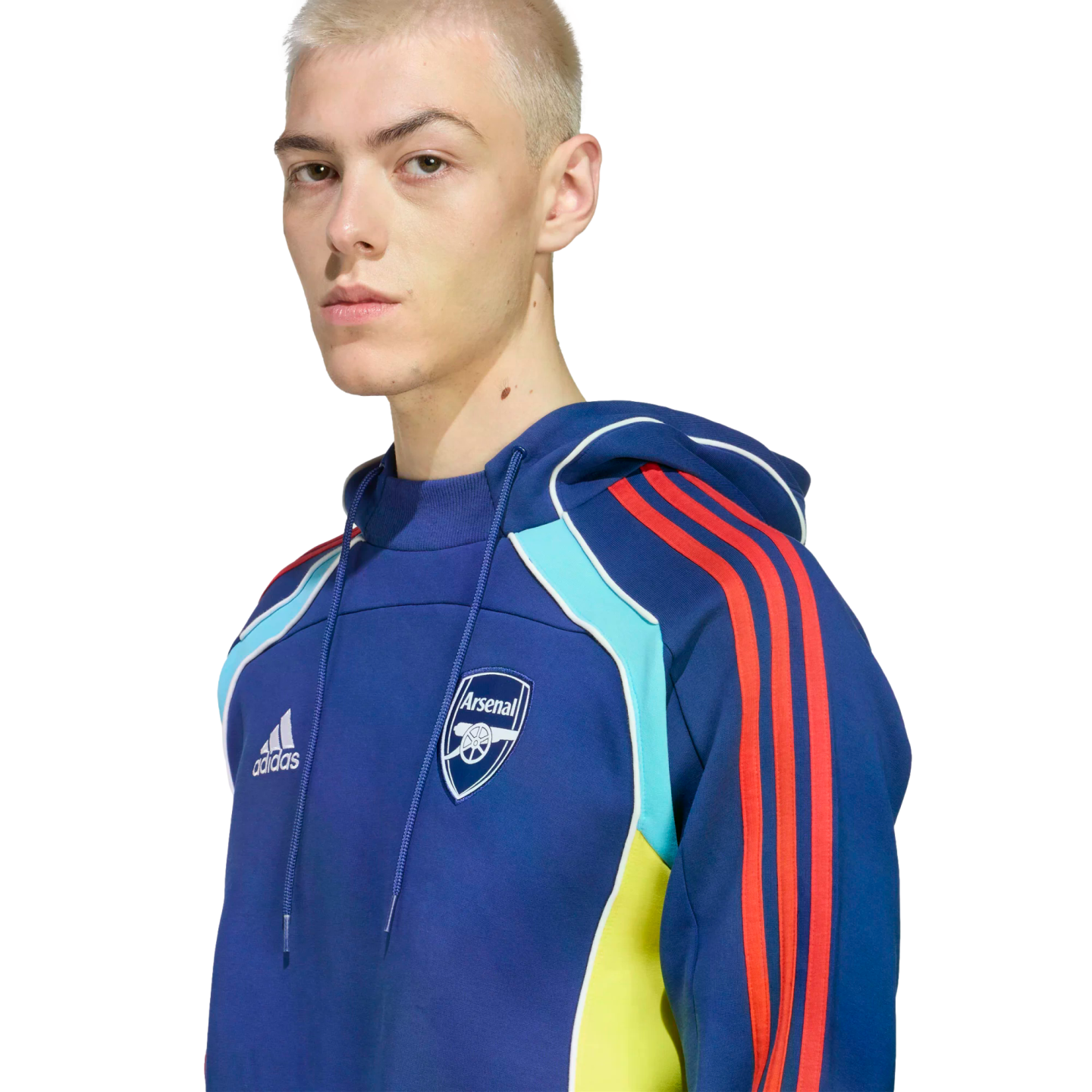 A person with short blonde hair wears a blue Adidas Arsenal FC hoodie with red stripes and yellow and light blue accents against a black background.