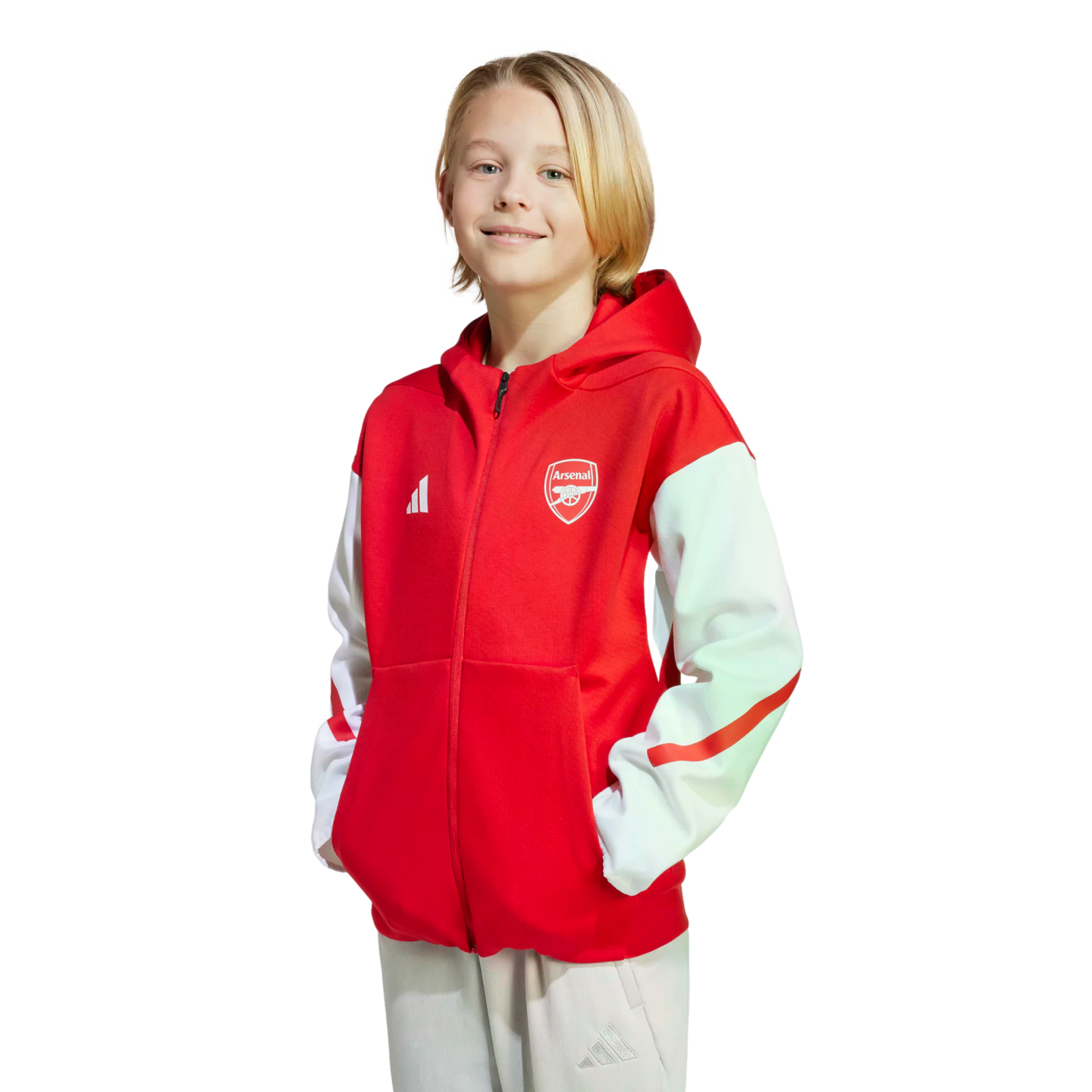 A young blonde boy smiles, wearing a red and white Arsenal zip-up hoodie against a black background.