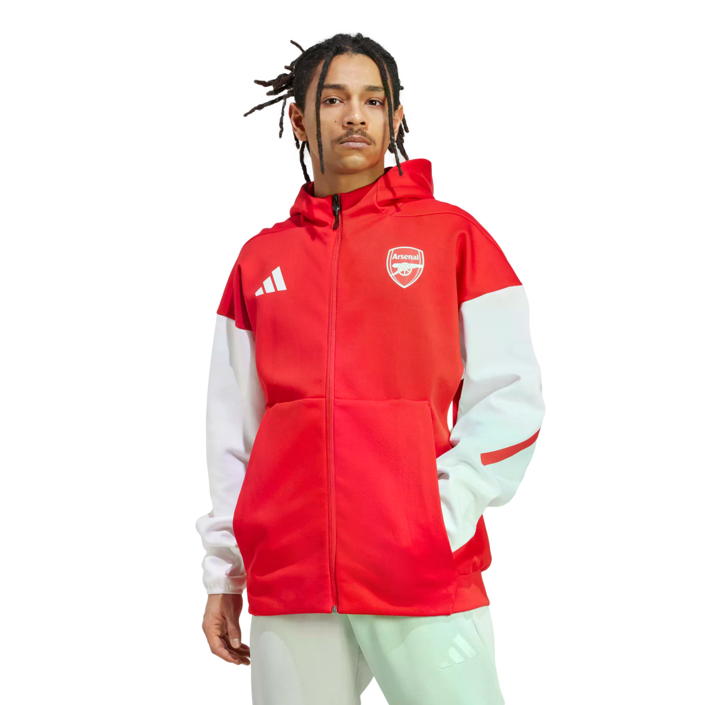 A man with dreadlocks wearing a red and white Adidas Arsenal zip-up hoodie and light-colored pants, posed against a white background.