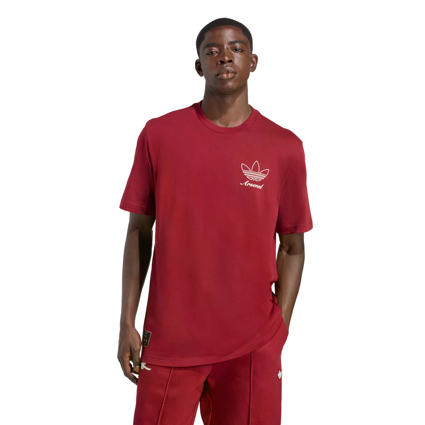 A man wearing a maroon t-shirt with a white Adidas trefoil logo and "Arsenal" text, paired with matching track pants, posed against a solid black background.