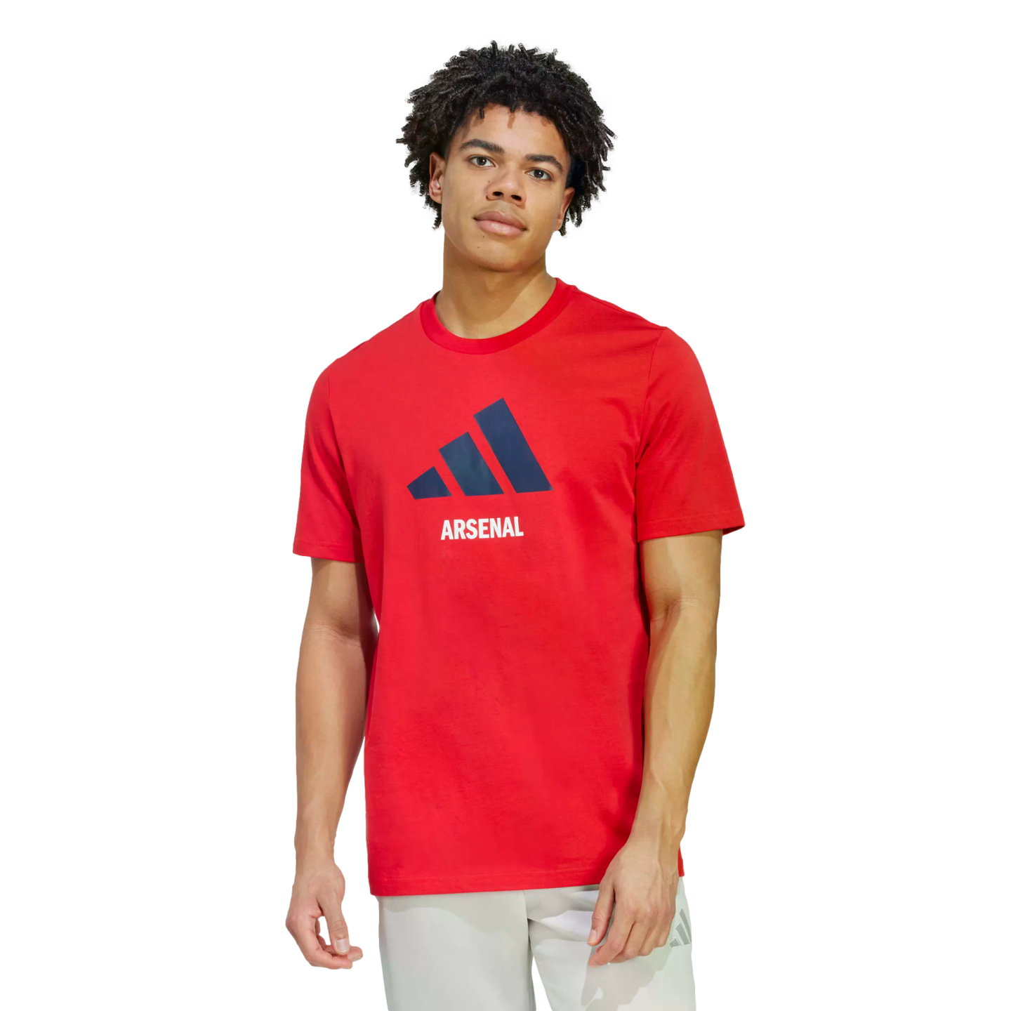 A man wears a red Adidas Arsenal t-shirt with a navy logo and white "ARSENAL" lettering. He is paired with light grey shorts against a solid black background.