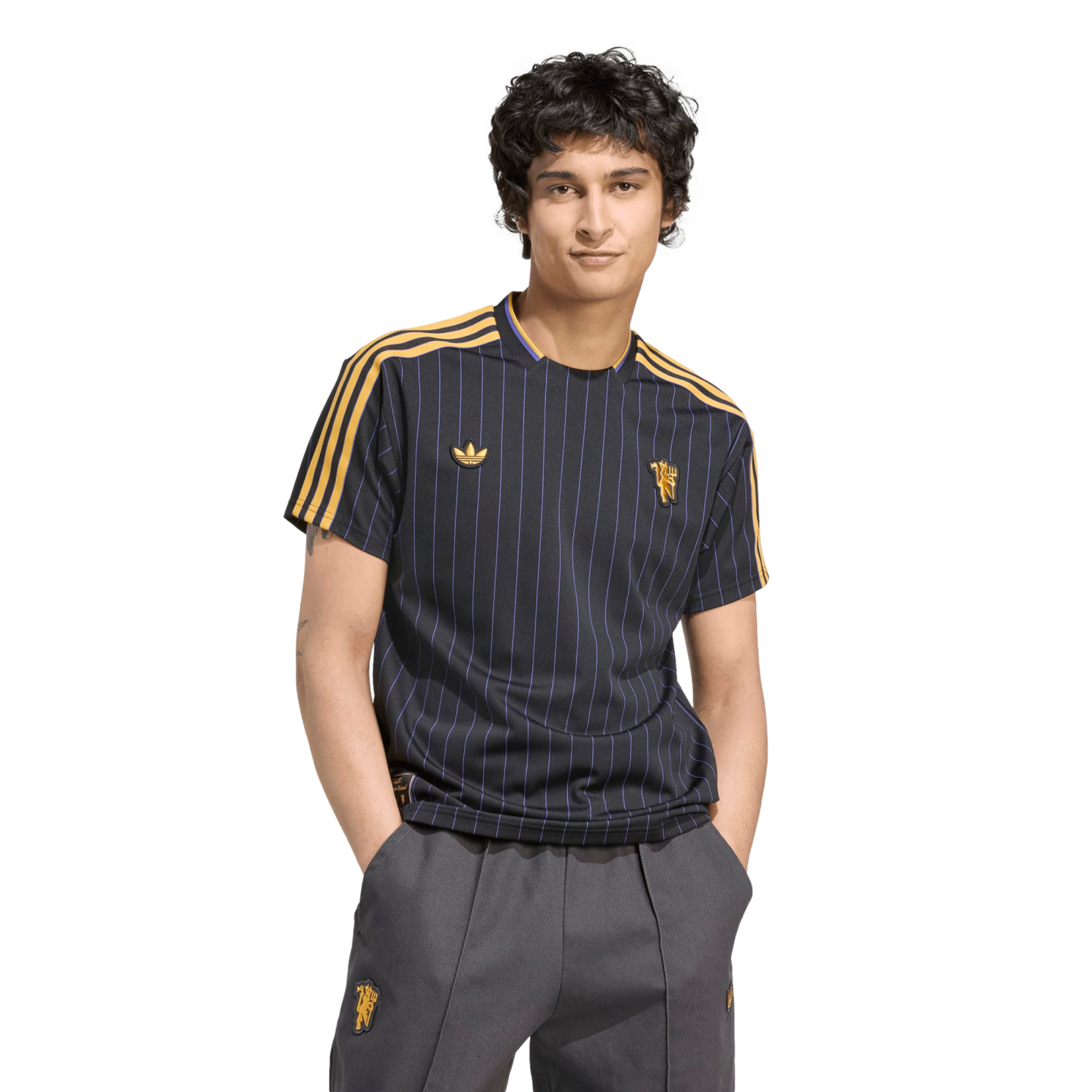 A man models a navy pinstriped Manchester United jersey and grey trousers against a black background.