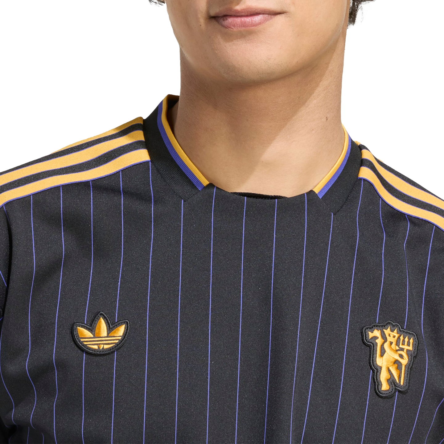 Close-up of a black jersey with purple pinstripes, gold shoulder stripes, an Adidas trefoil logo, and a Manchester United crest.
