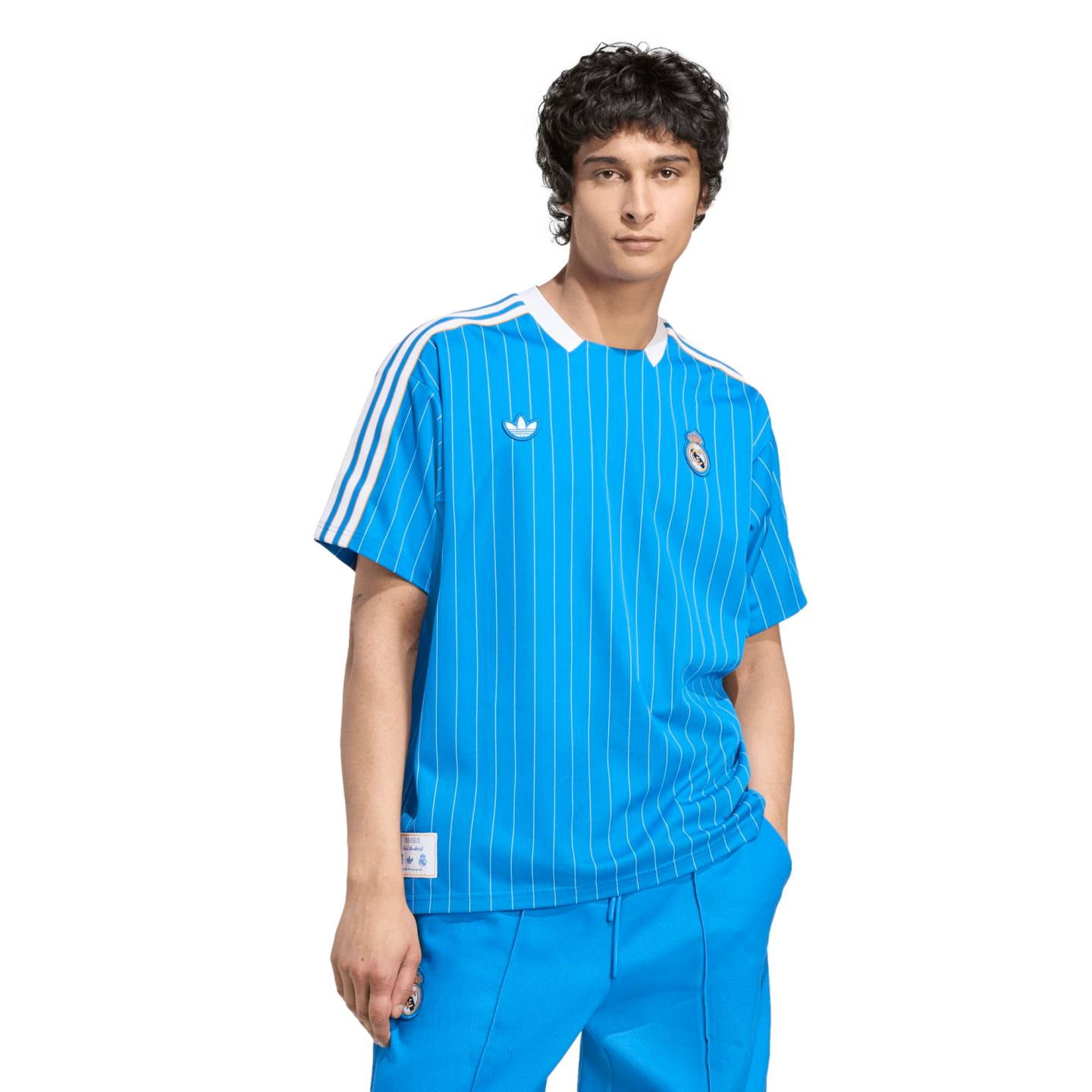 A young man wearing a bright blue pinstriped Real Madrid Adidas jersey and matching pants against a solid black background.