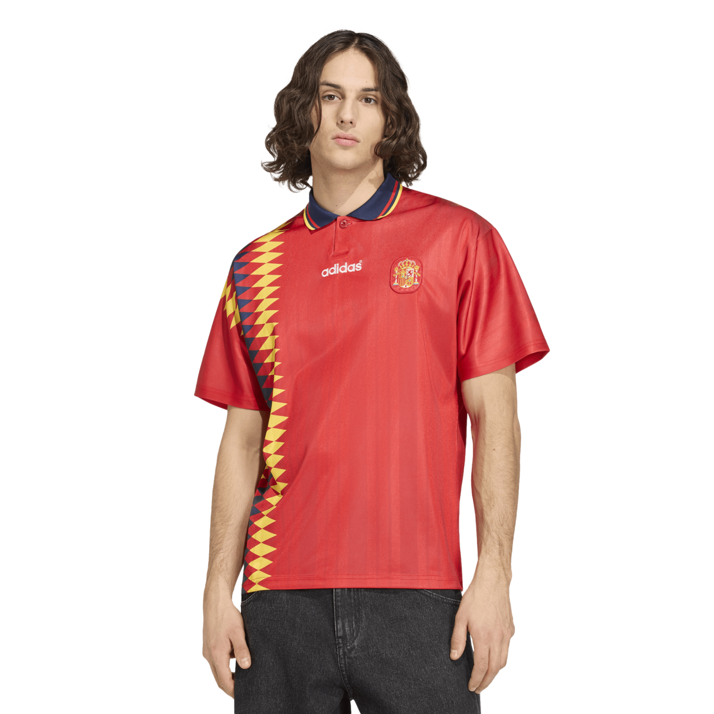 A man wearing a red Adidas Spain soccer jersey with a yellow and blue diamond pattern on the side, paired with dark jeans.