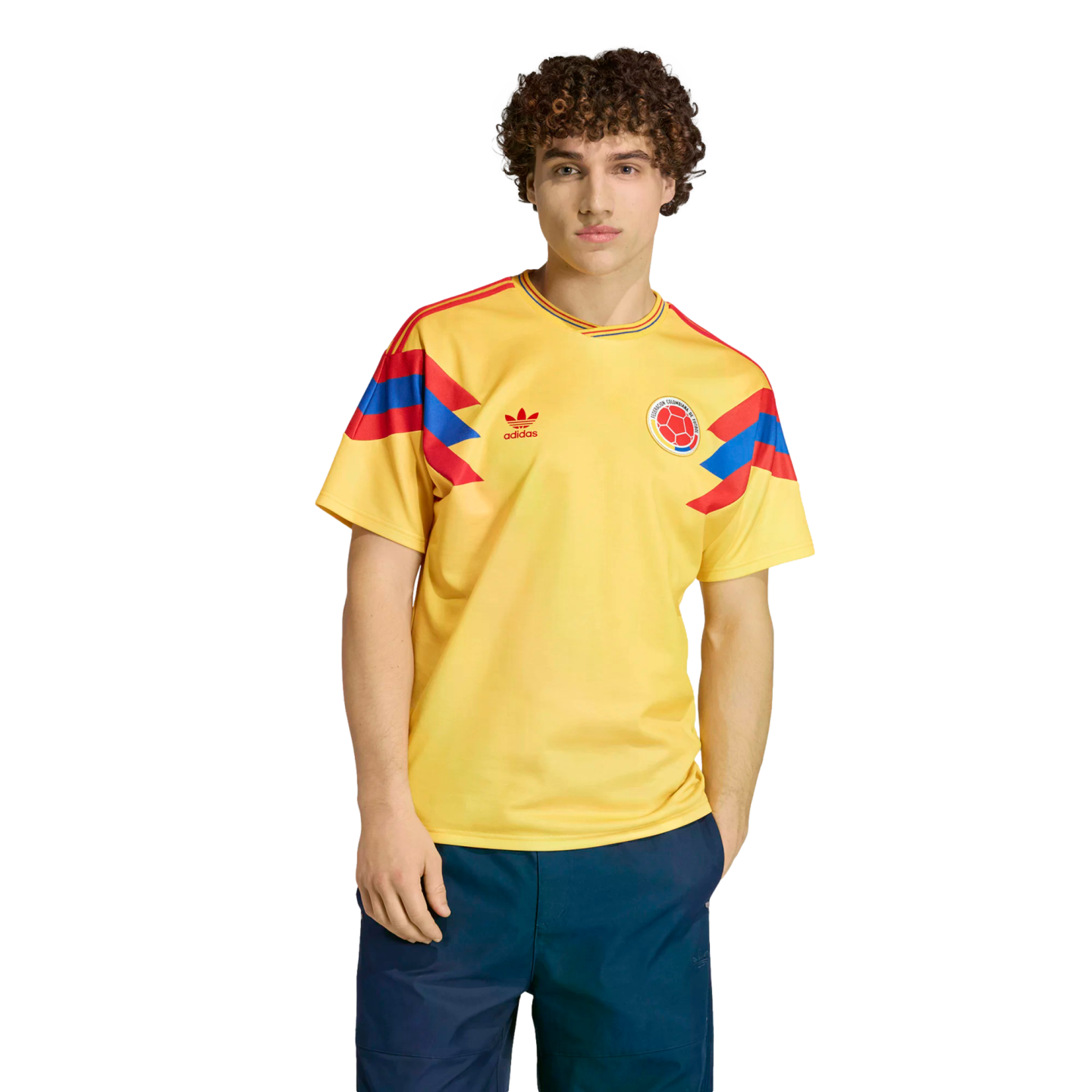 A man modeling a yellow Colombia national football team jersey with red and blue accents on the sleeves, standing against a black background.