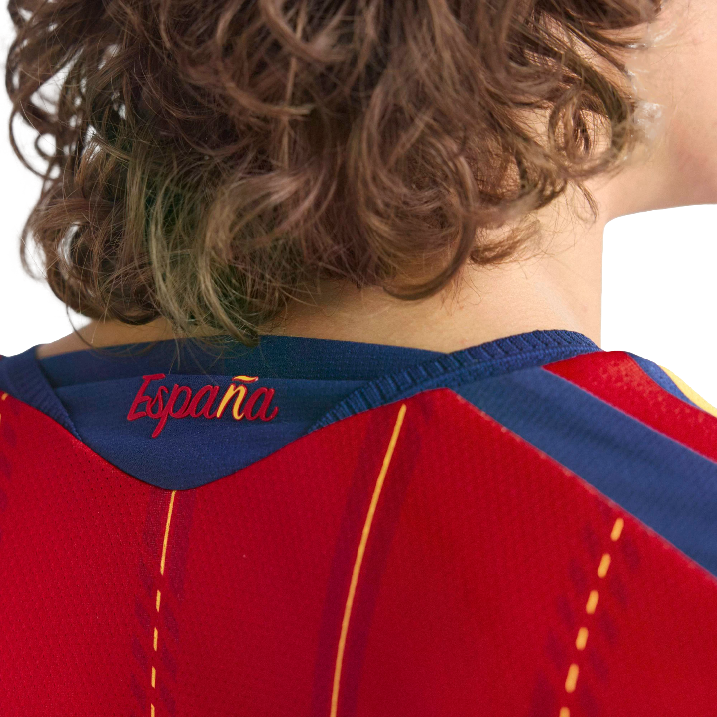 Close-up of the back of a person with curly hair wearing a red Spanish football jersey with "España" scripted on the blue neckline.