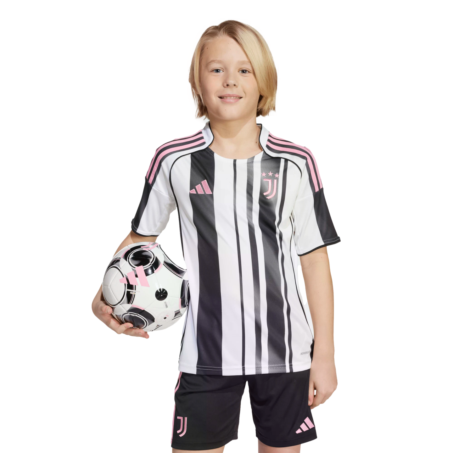 A smiling child with blonde hair wearing a black, white, and pink soccer uniform, holding a matching soccer ball under one arm against a white background.