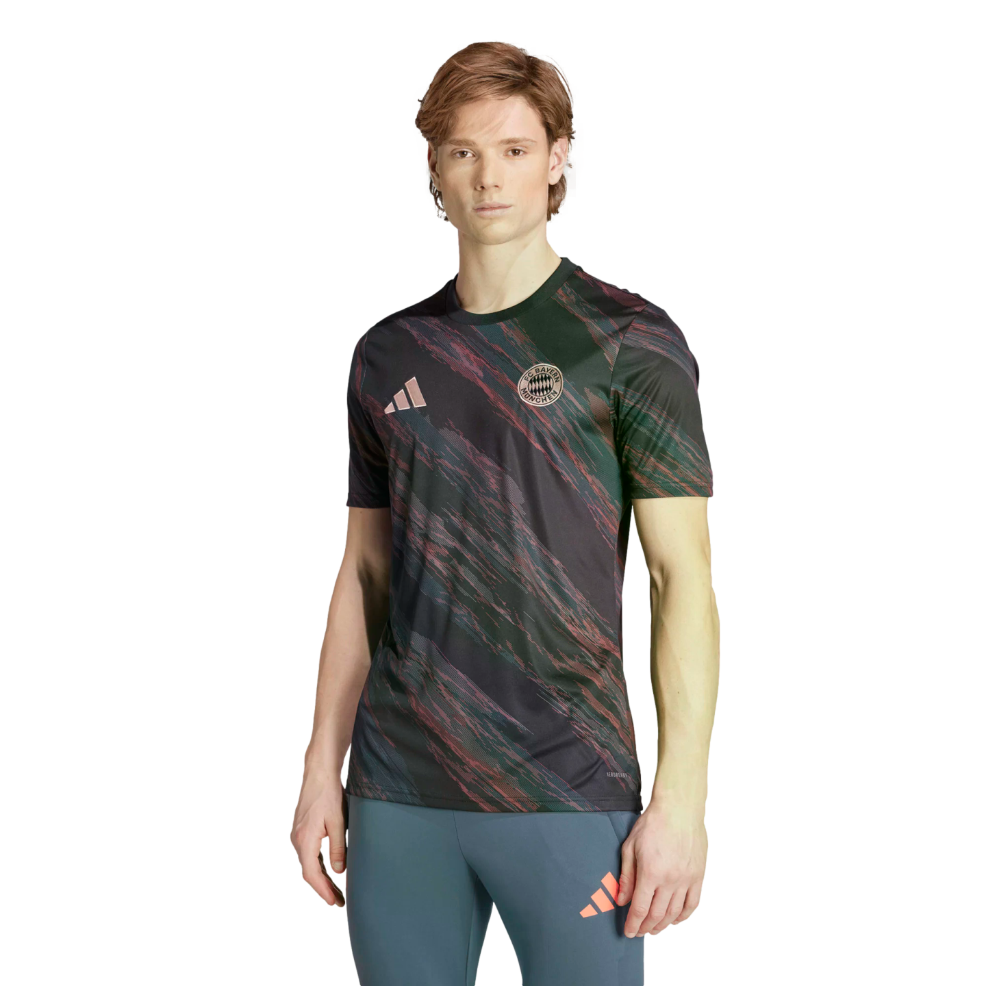 A man models an Adidas FC Bayern Munich jersey with a dark pink and green brushstroke pattern and blue athletic leggings against a white background.