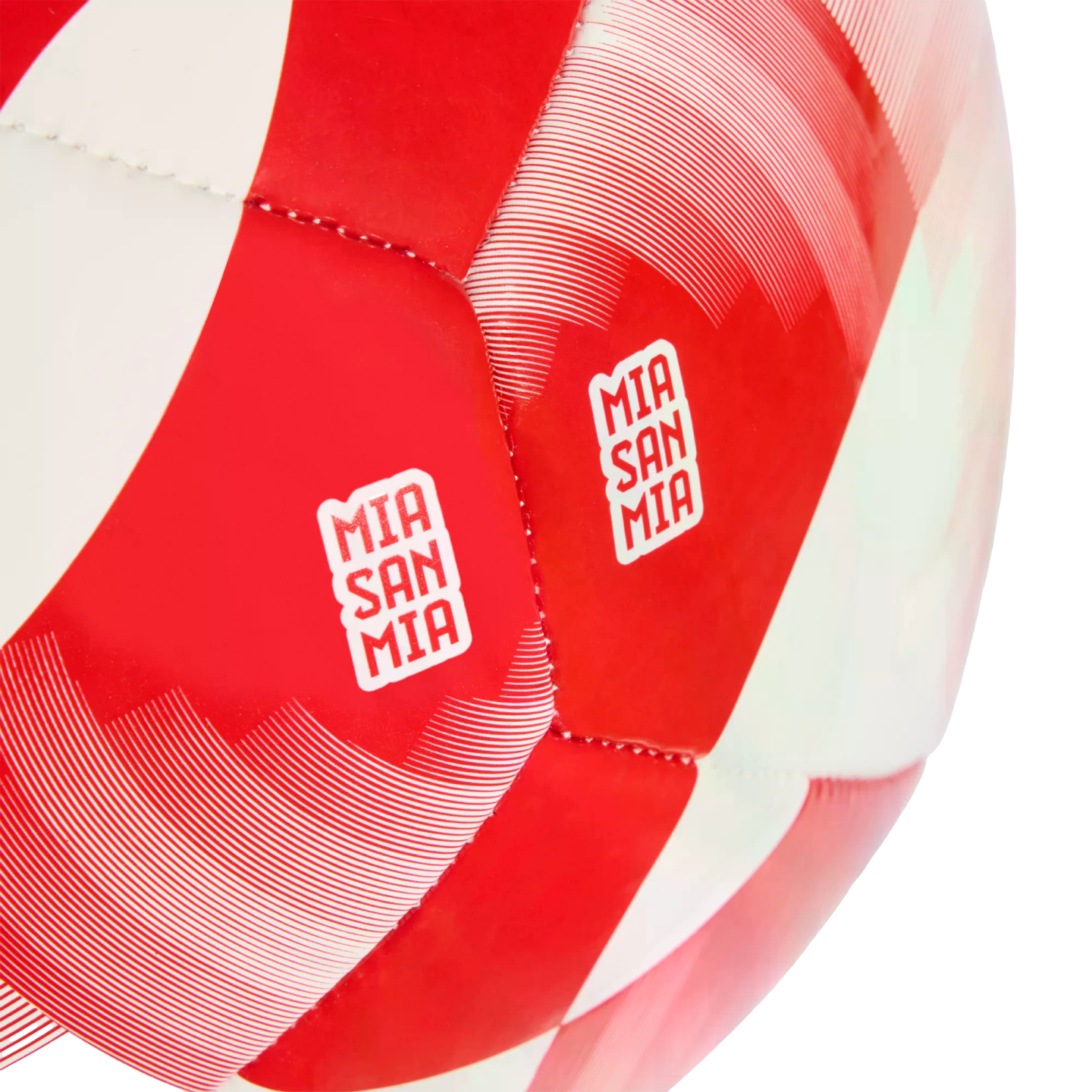Close-up of a red and white soccer ball with "MIA SAN MIA" logos on red panels. The ball features a geometric pattern with thin white decorative lines.