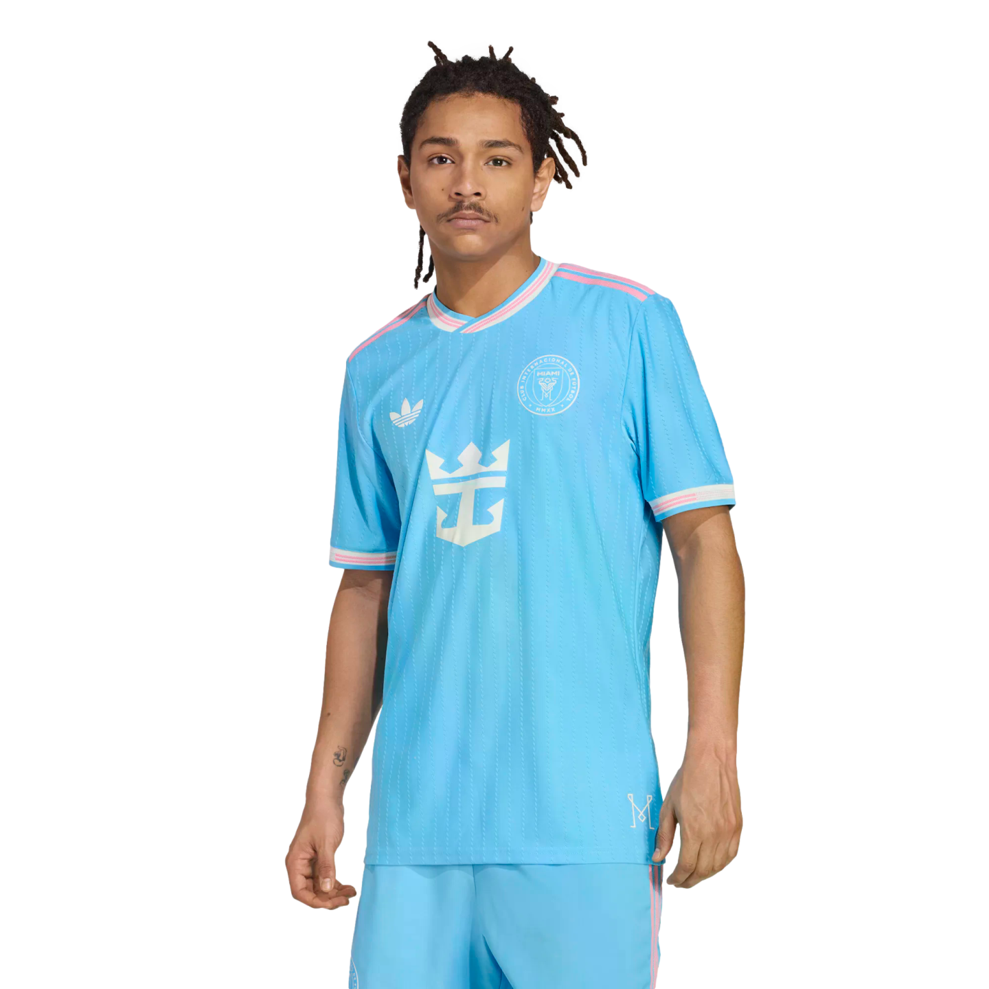 A man with dreadlocks models a light blue Inter Miami CF soccer jersey with pink trim and a Royal Caribbean logo against a white background.