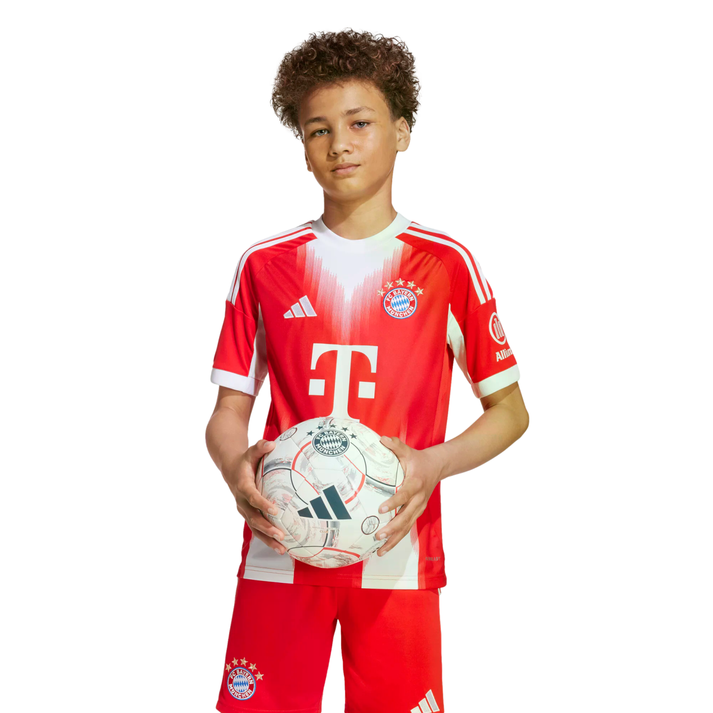 A young boy with curly hair wears a red and white FC Bayern Munich soccer uniform while holding a soccer ball against a plain white background.