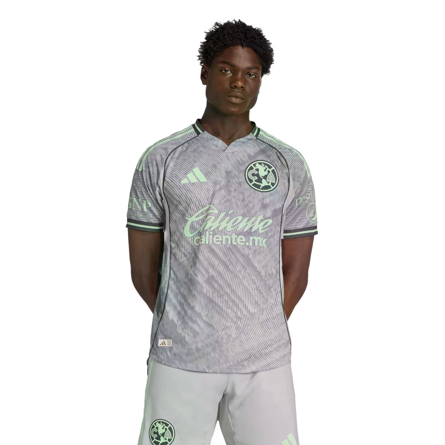 Male model wearing a light gray and mint green Club América soccer jersey and matching shorts, standing against a solid black background.