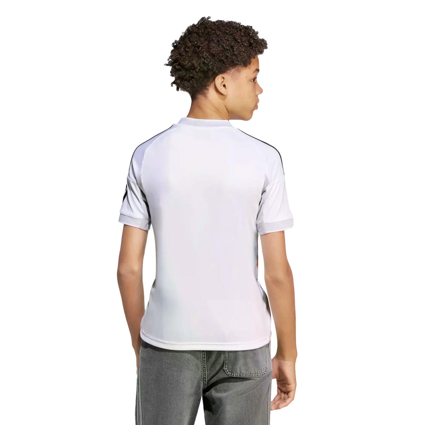 Back view of a youth with curly hair wearing a white athletic jersey with black shoulder stripes and grey jeans against a white background.