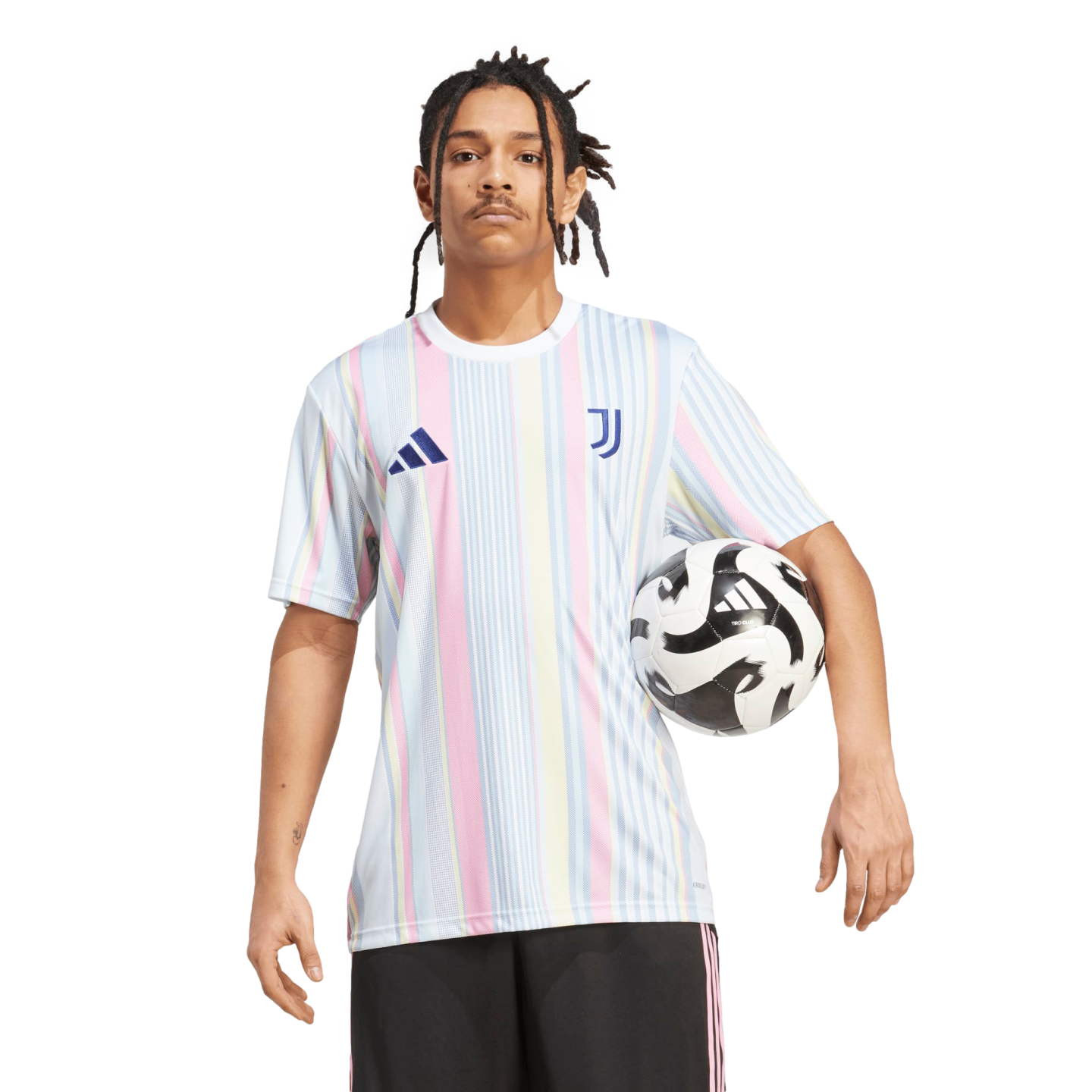 A man with dreadlocks wears a pastel-striped Juventus soccer jersey and black shorts, holding a soccer ball against a white background.