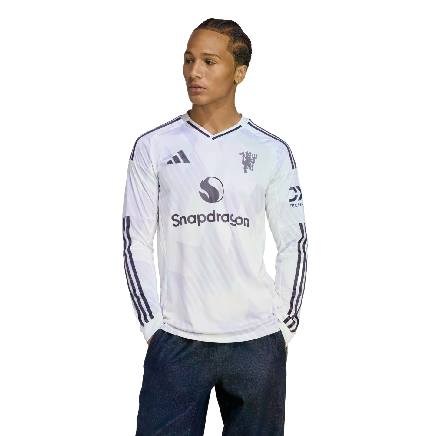 A man wearing a white long-sleeve Manchester United jersey with a Snapdragon logo, looking to the side against a black background.
