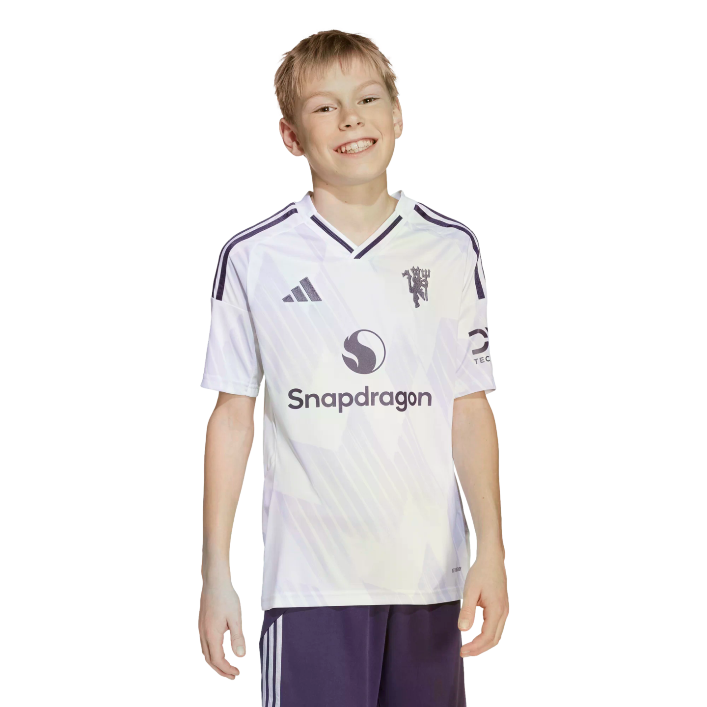 A smiling boy wearing a white and purple Manchester United soccer jersey with a Snapdragon logo, standing against a black background.