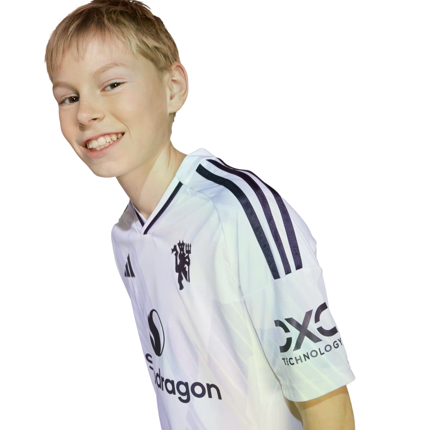 A young person with blonde hair smiles while leaning forward, wearing a white soccer jersey featuring several logos. The image is set against a solid black background.