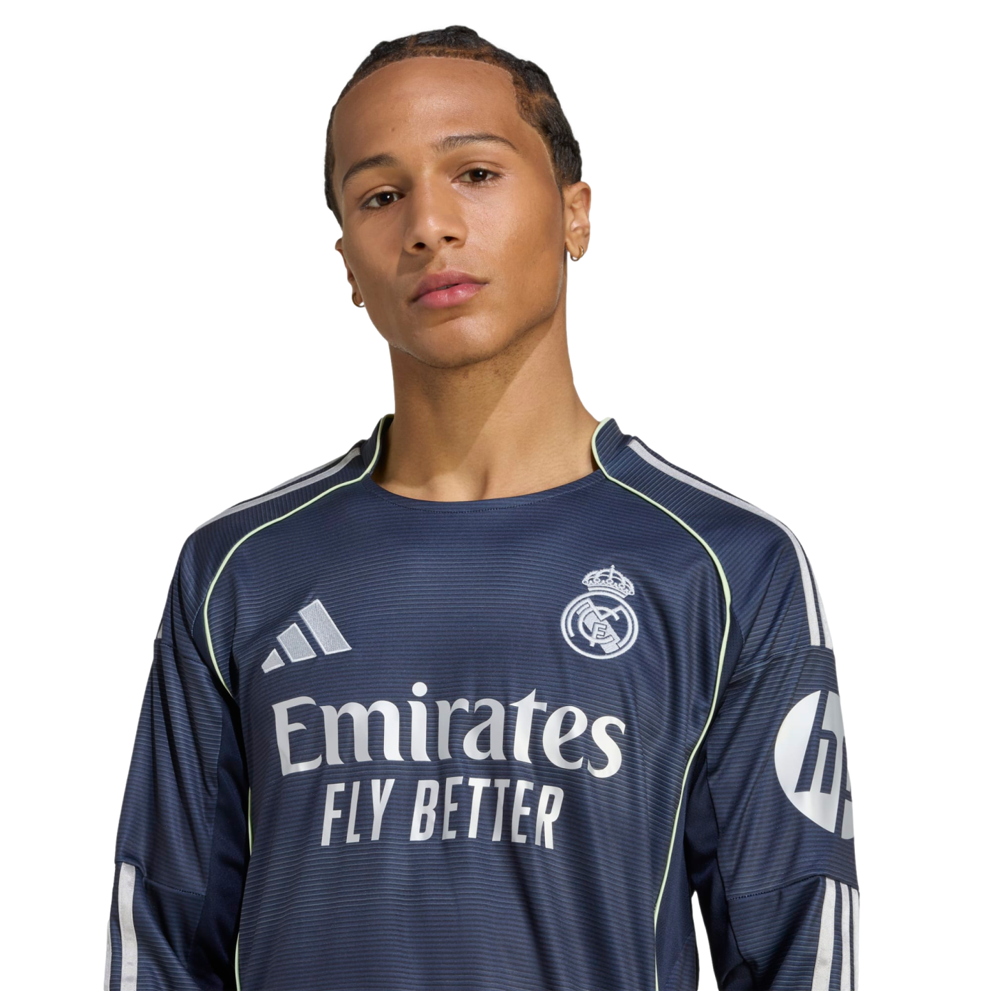 Portrait of a man with braided hair wearing a navy blue Real Madrid soccer jersey against a white background.