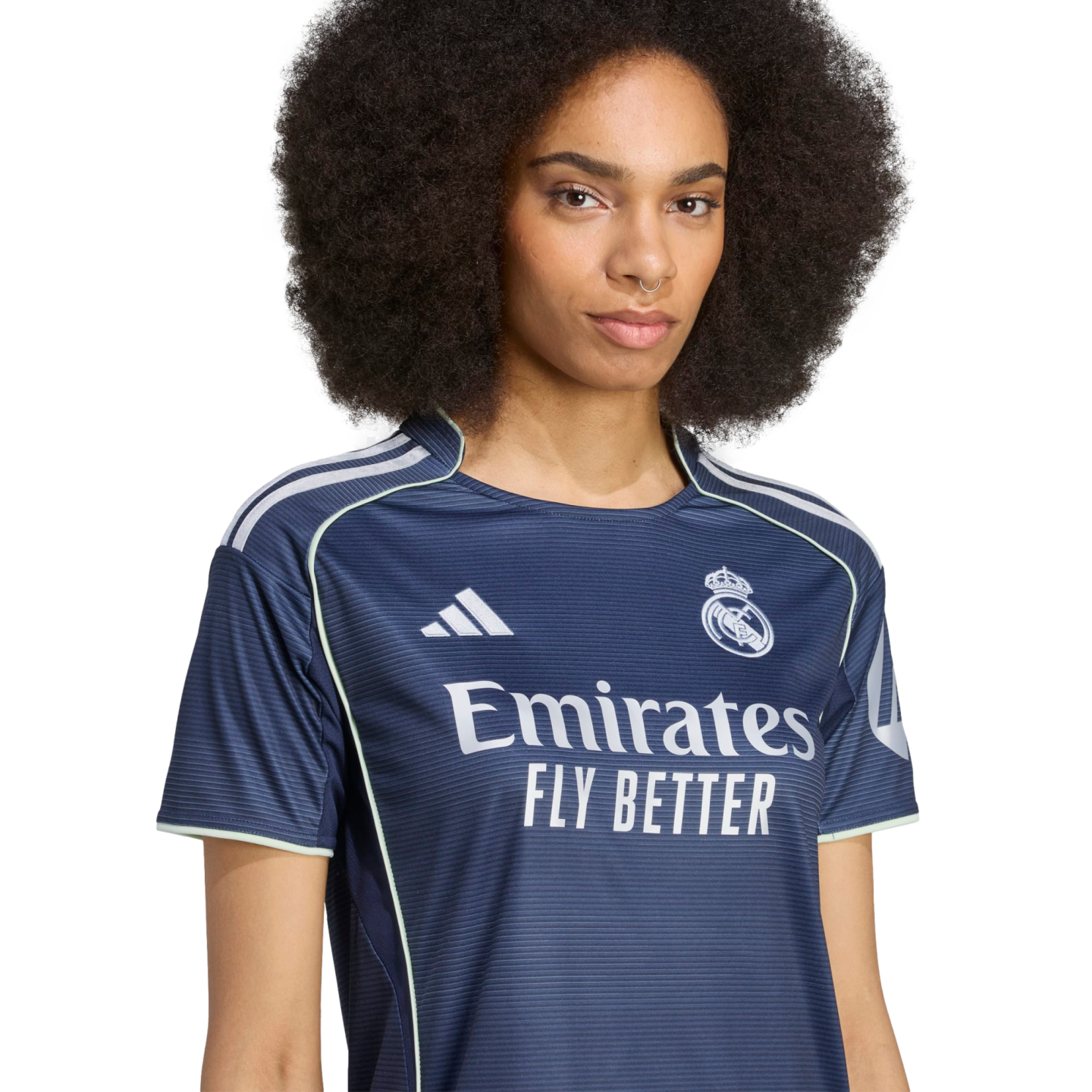 A woman with a large afro wears a navy blue Real Madrid soccer jersey with white trim and "Emirates Fly Better" sponsor text.