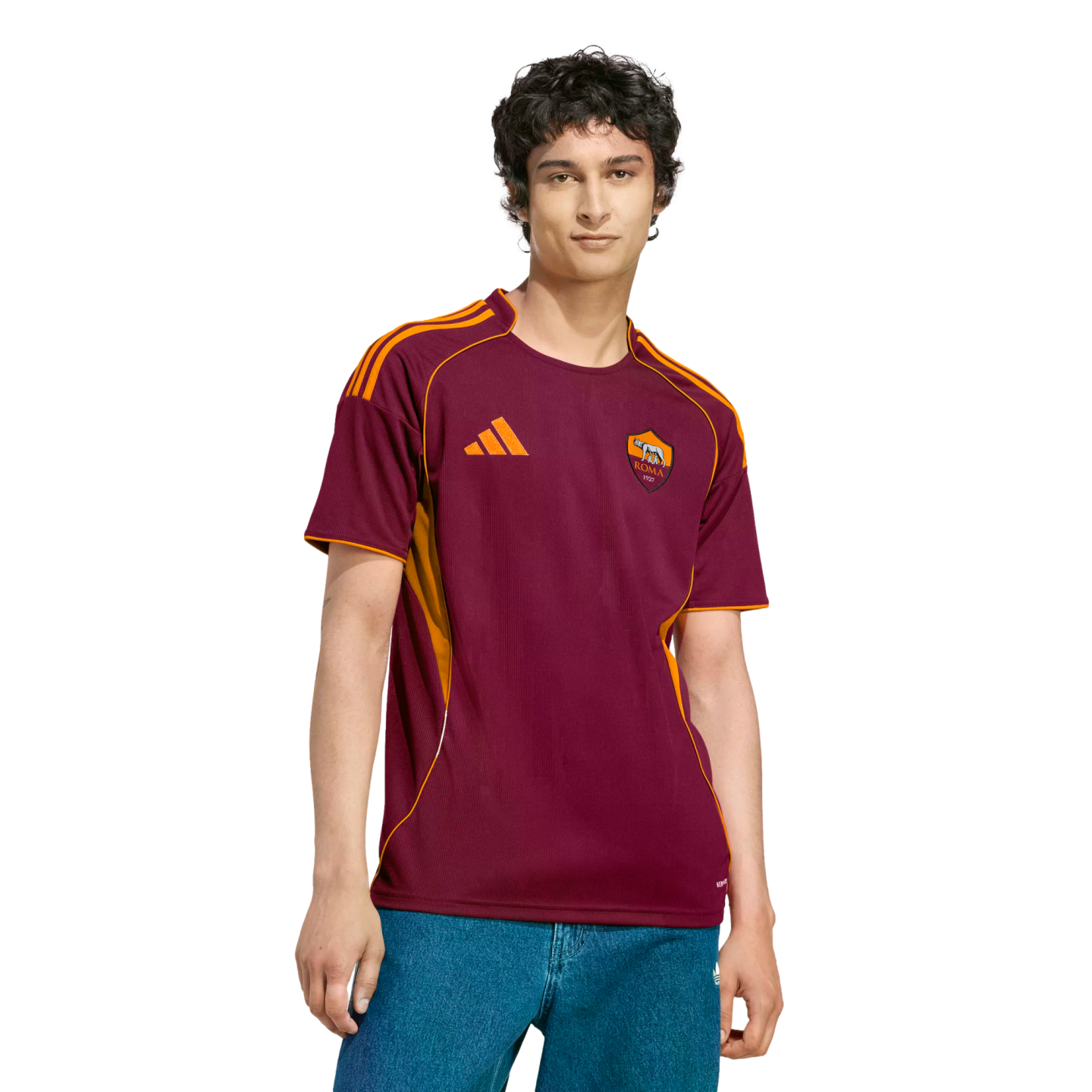 A man wearing a burgundy and orange AS Roma football jersey and blue jeans against a black background.