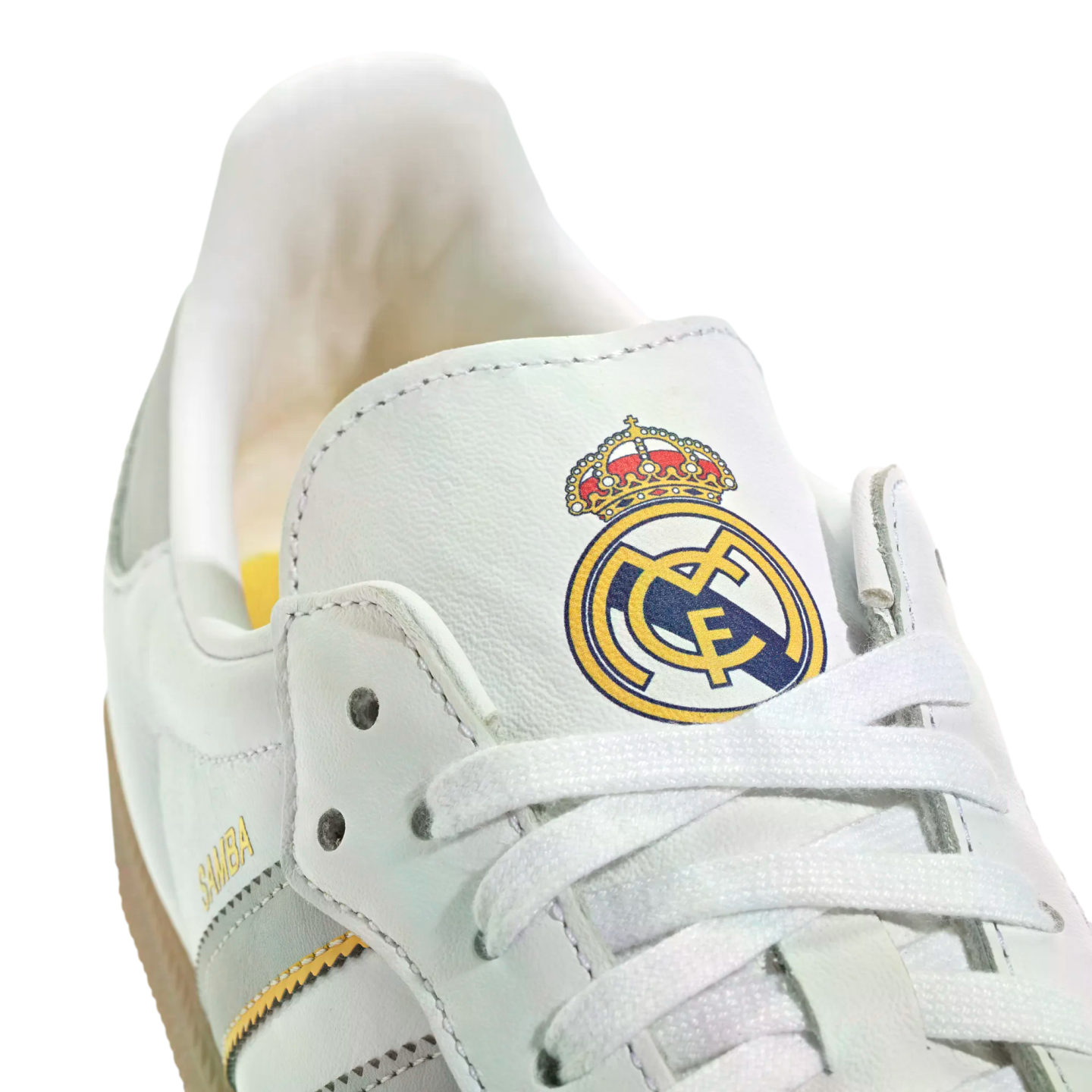 Close-up of a white Adidas Samba sneaker featuring the Real Madrid club crest on the tongue and gold "SAMBA" lettering.