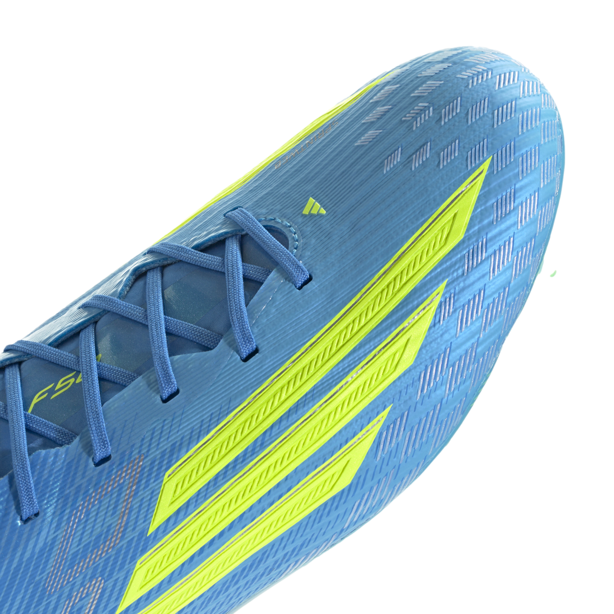 A close-up of a light blue Adidas F50 soccer cleat featuring three bold neon yellow stripes on the side. The shoe has a textured, ribbed upper with blue laces and a shimmering checkered pattern near the toe, shown against a black background.