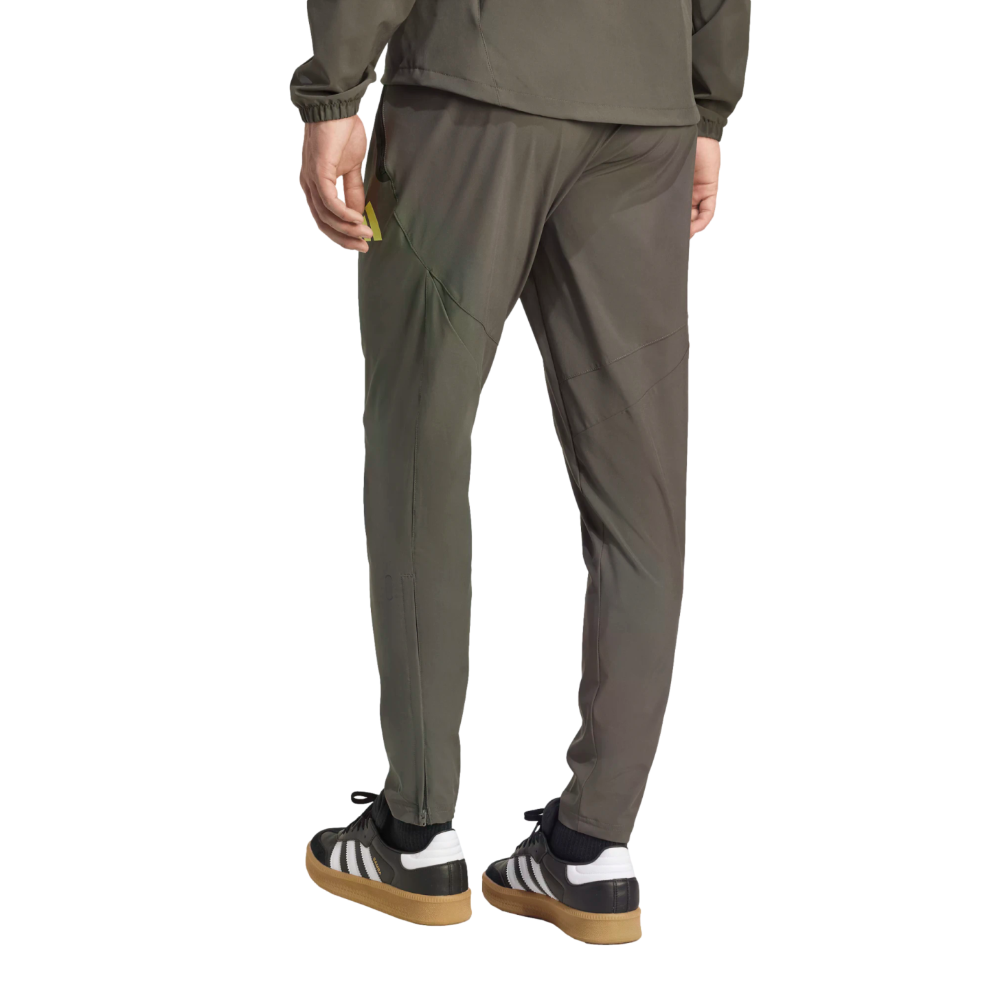 Rear view of a person wearing olive green athletic pants and jacket with black Adidas Samba sneakers.