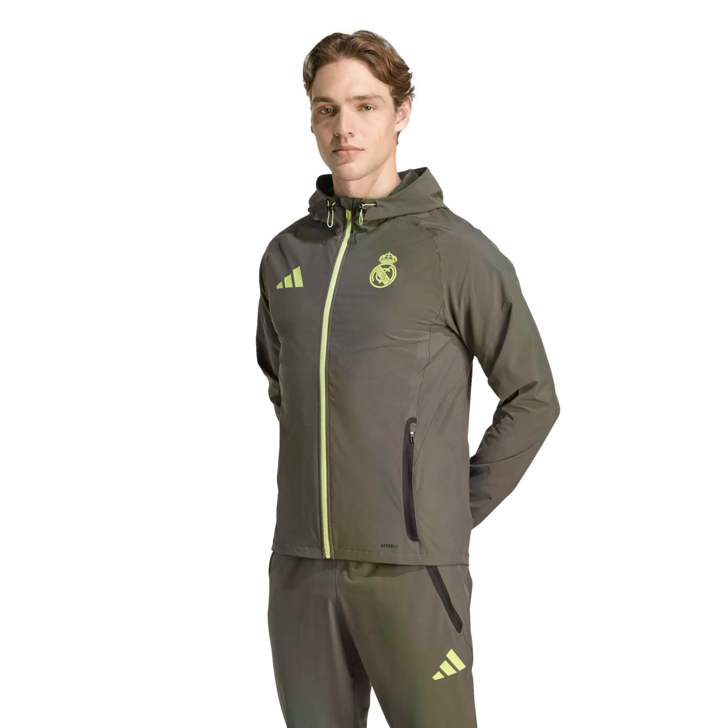 Man in an olive green Real Madrid Adidas tracksuit with neon yellow accents, standing against a black background.