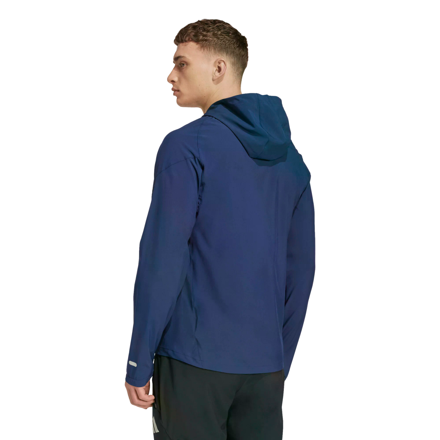 A man is shown from the back and side, wearing a navy blue hooded athletic jacket and black shorts against a solid black background.