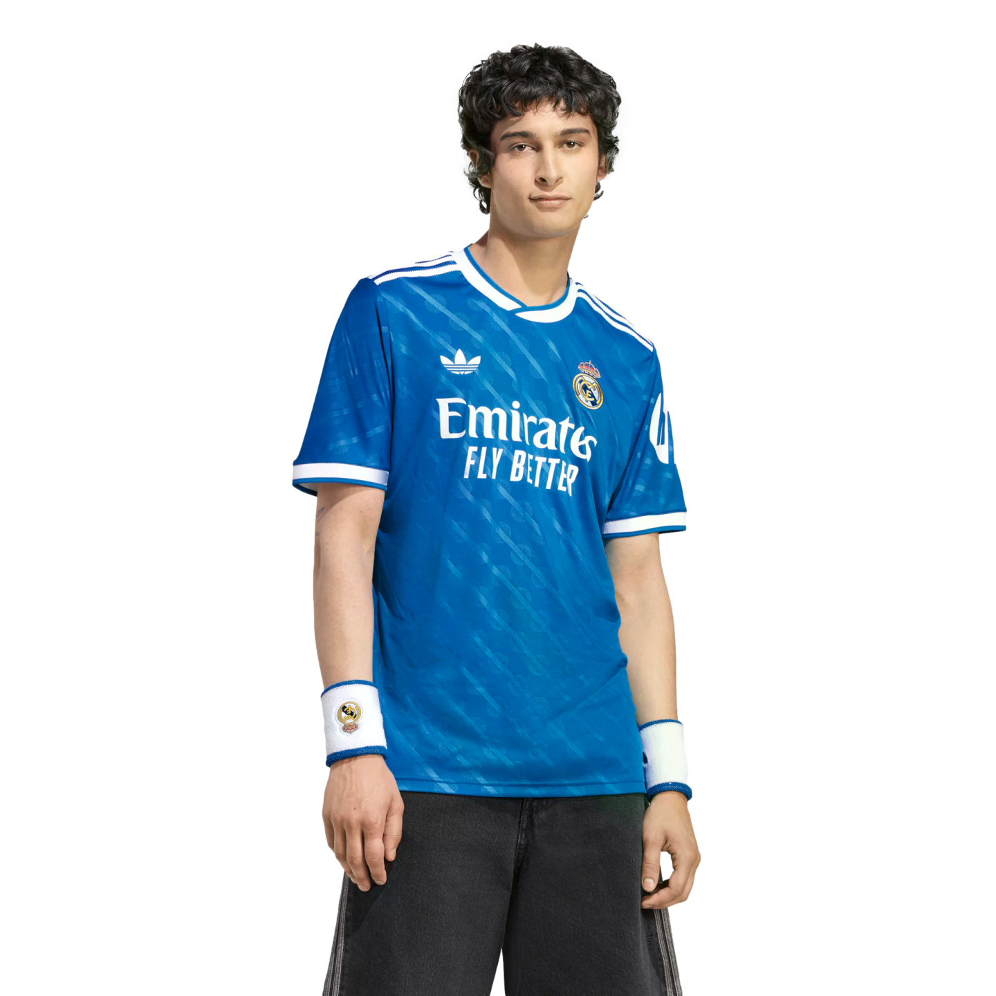 A man wearing a blue Real Madrid soccer jersey with white accents and matching wristbands, standing against a solid black background.