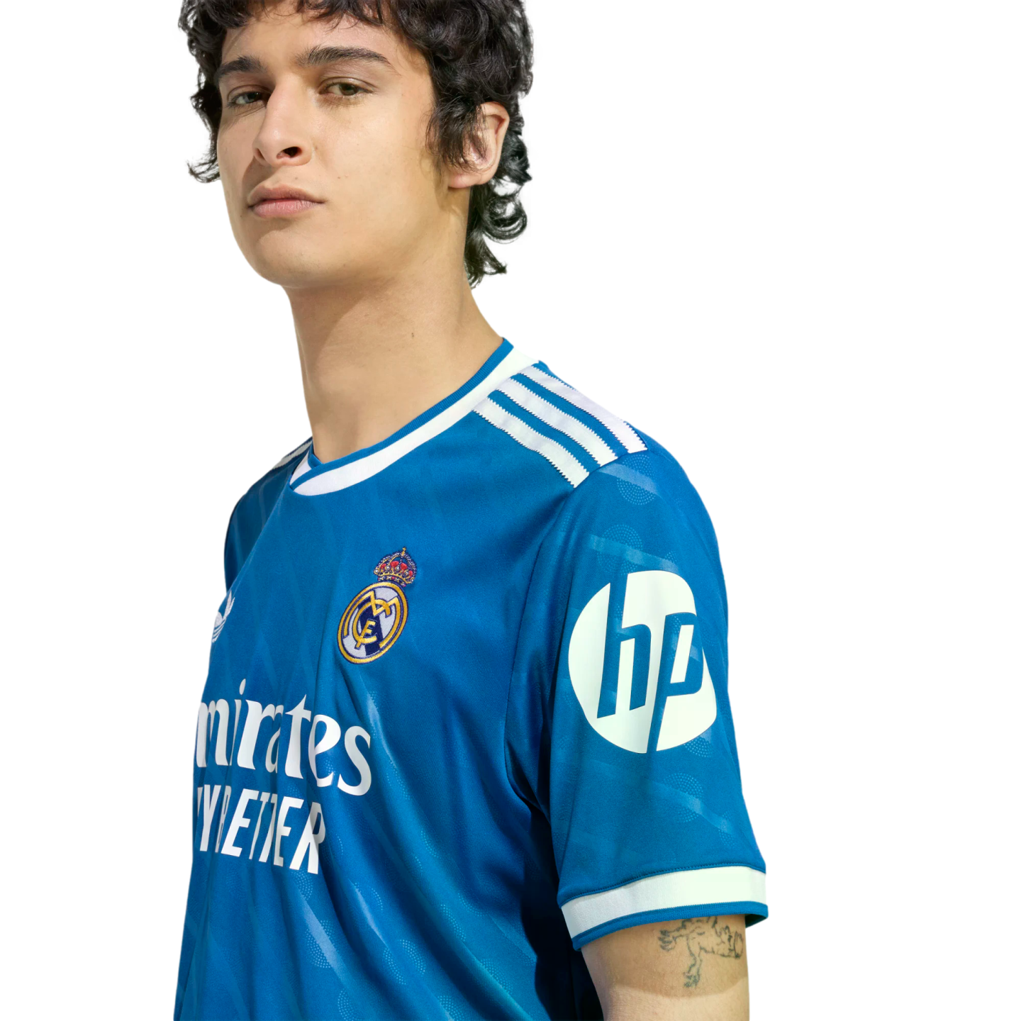 Young man wearing a blue Real Madrid soccer jersey with white trim and sponsor logos, posed against a black background.
