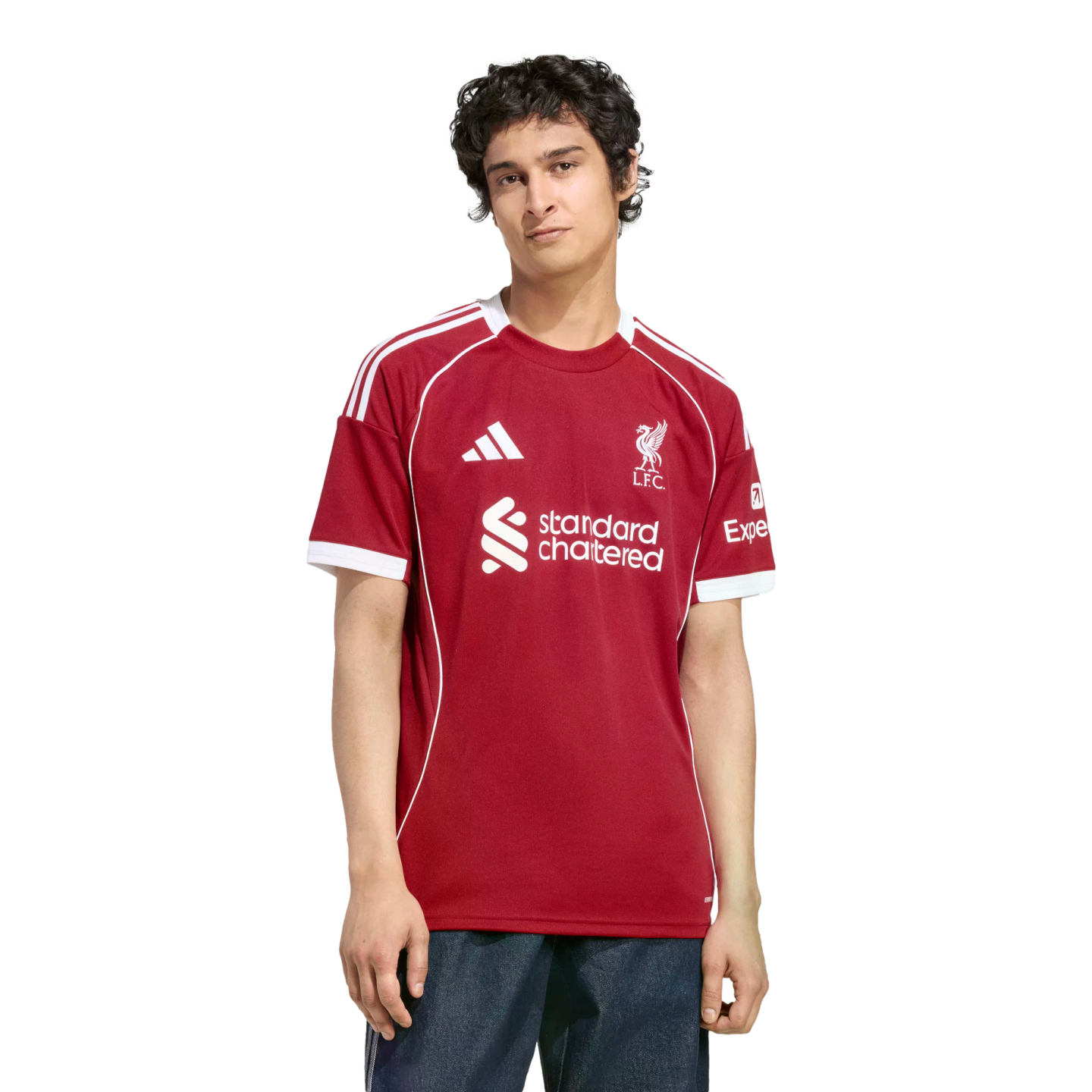 A young man modeling a red Liverpool FC jersey with white trim and sponsor logos, set against a solid black background.