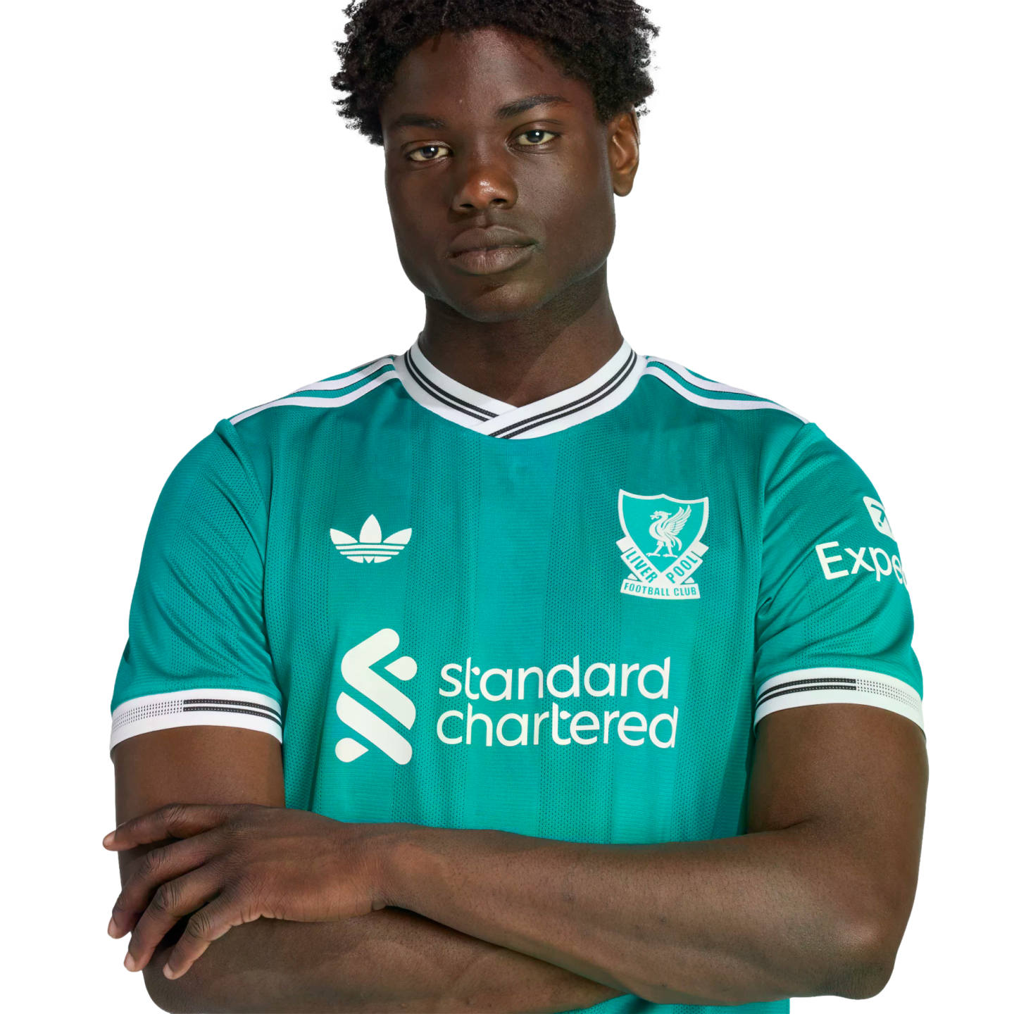 A young Black man with arms crossed wearing a teal Liverpool FC soccer jersey against a black background.