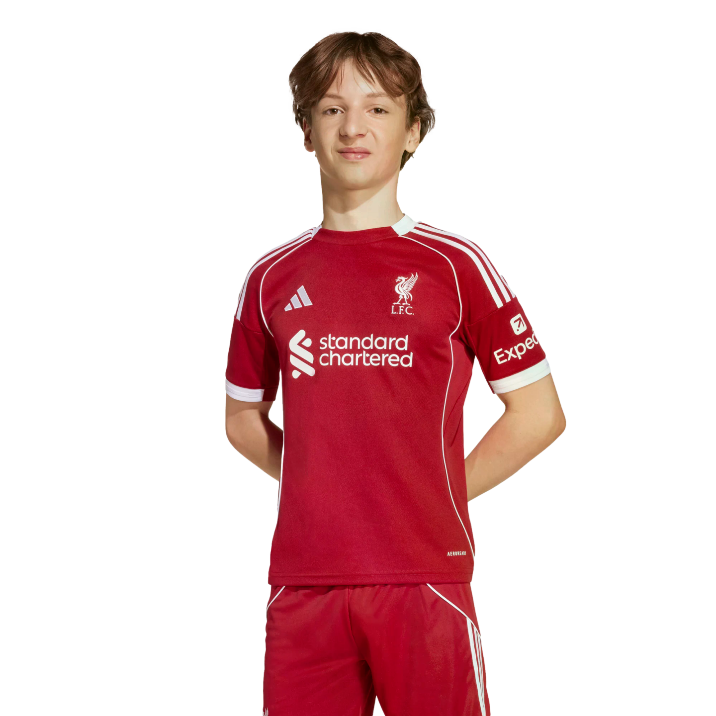 Young man wearing a red Liverpool FC soccer kit with white details and sponsor logos, standing against a solid black background.