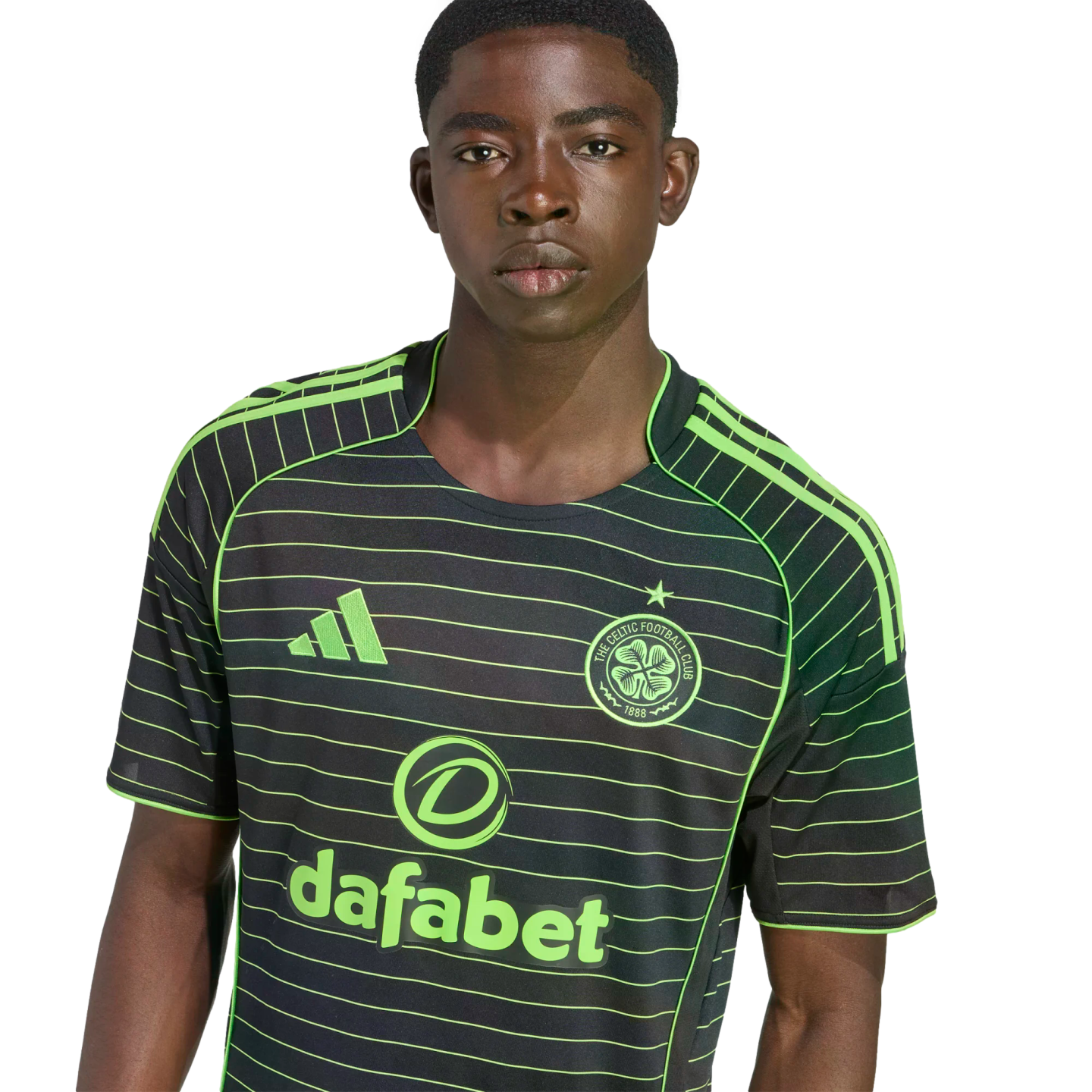 A young Black man wearing a black and neon green striped Celtic FC away jersey against a black background.