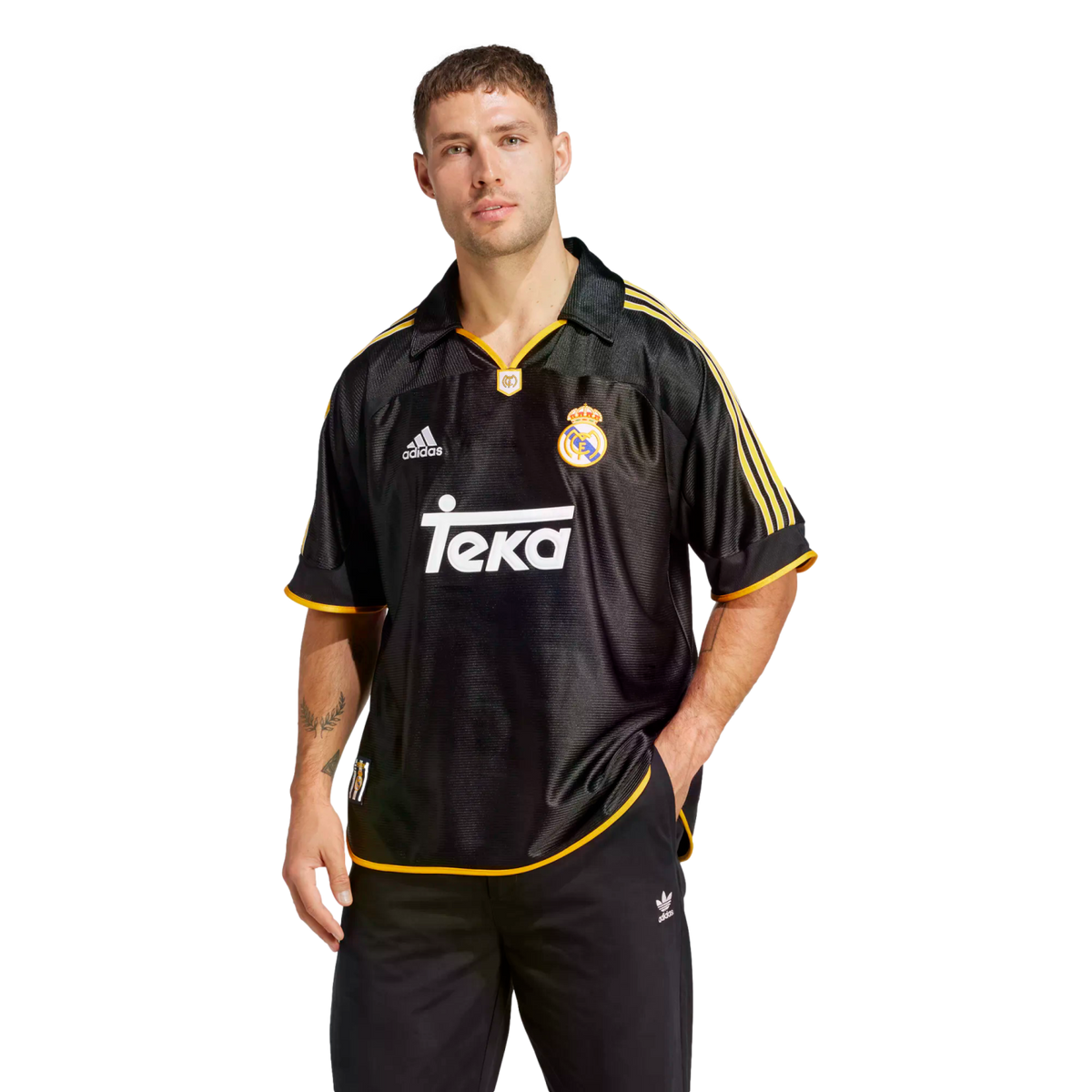 A man modeling a black and gold retro Adidas Real Madrid soccer jersey with a white Teka sponsor logo across the chest.