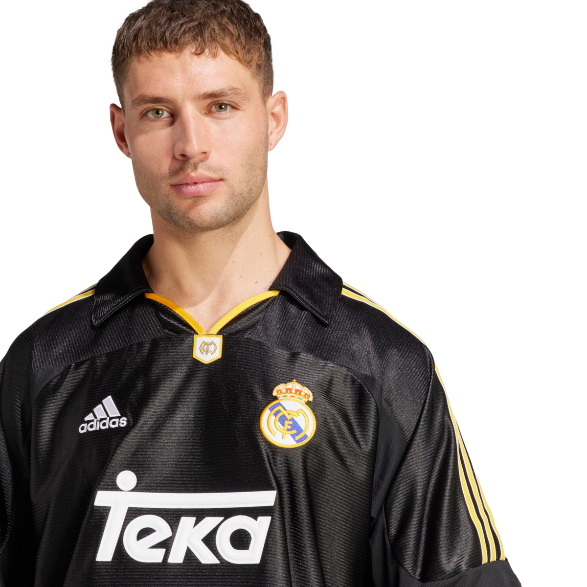 A portrait of a man with light green eyes and short brown hair, wearing a vintage-style black Real Madrid away jersey with yellow accents. The jersey features the adidas logo, the club crest, and the "Teka" sponsor name in white. He is looking directly at