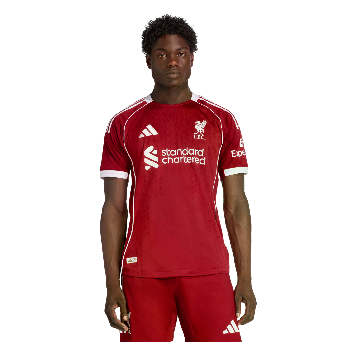 A young man wearing the red 2024-25 Liverpool F.C. home soccer kit, standing against a black background.