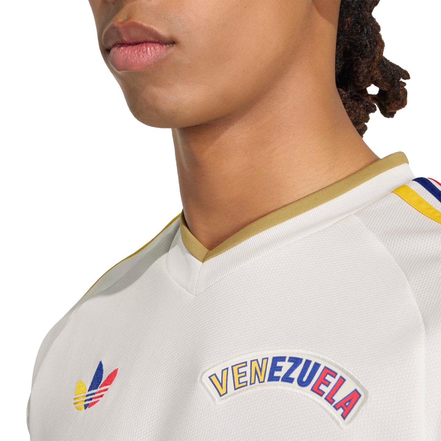 Close-up of a person wearing a white Adidas Venezuela jersey with a gold collar and colorful logos on the chest, set against a black background.
