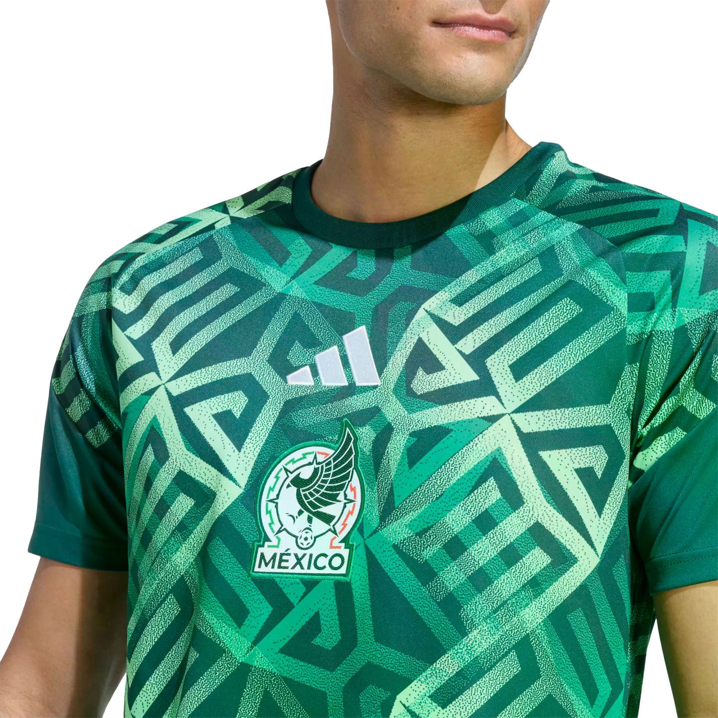 A man wears a green Adidas Mexico soccer jersey featuring a bold, geometric pattern inspired by ancient civilizations and the official team crest.