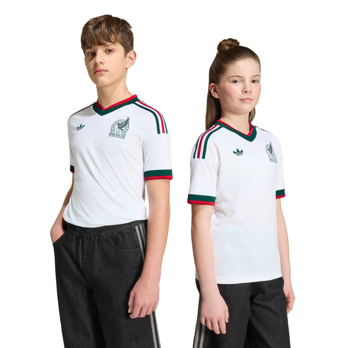 Two youths wearing white Mexico national team soccer jerseys with green and red trim and black pants, standing against a solid black background.