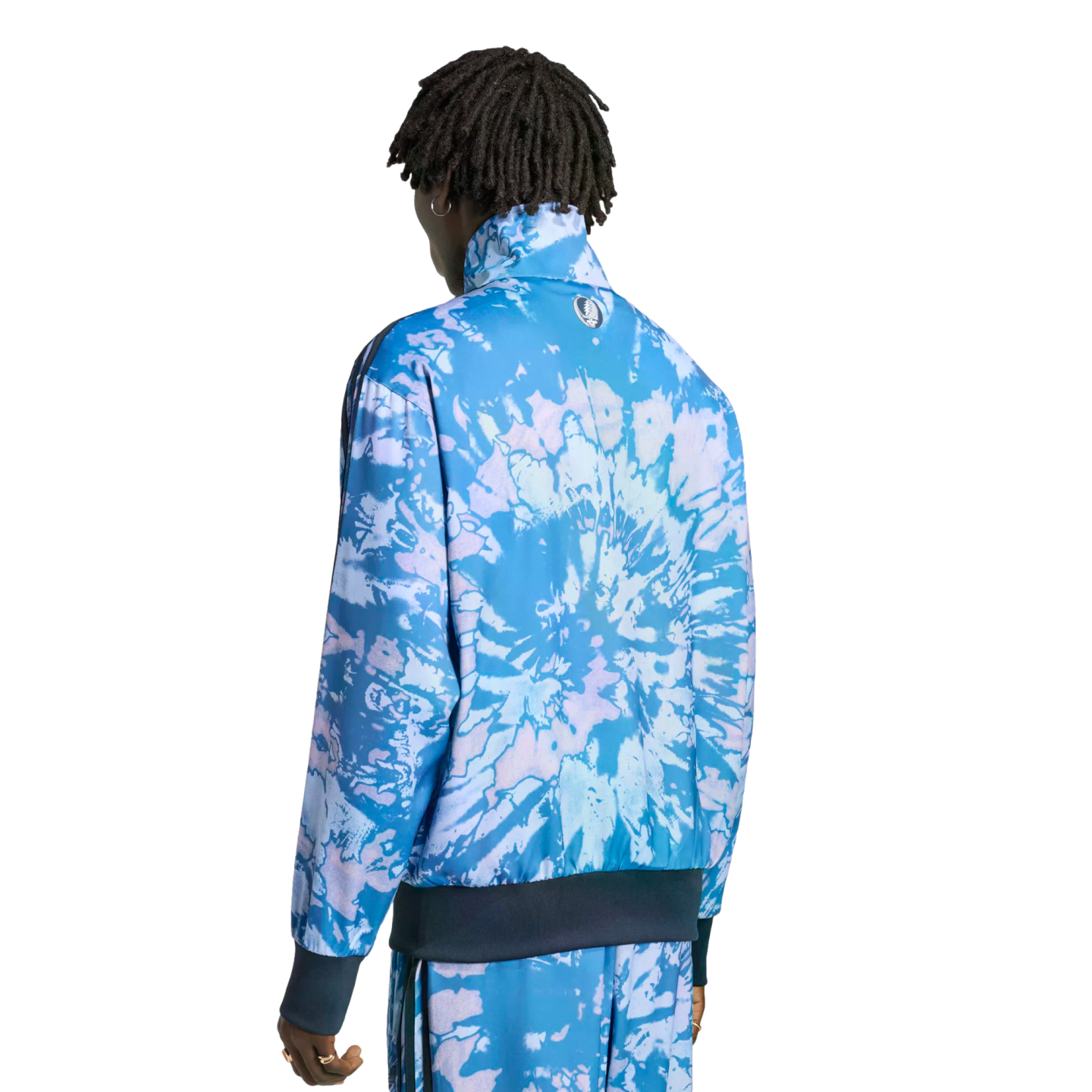 A person from behind wearing a blue and purple tie-dye tracksuit with a small circular logo on the jacket back. Solid black background.
