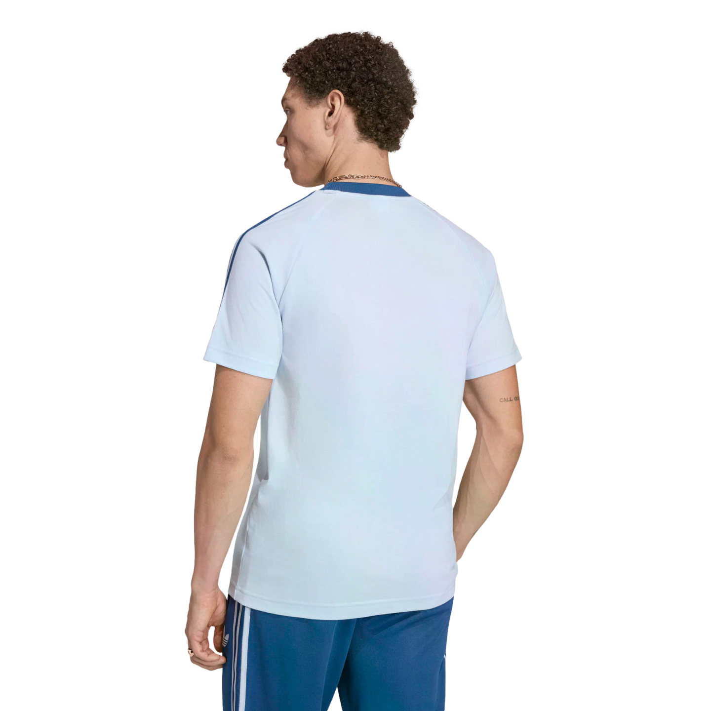 A man from behind, wearing a light-blue short-sleeved t-shirt with dark blue shoulder stripes and dark blue shorts with white side stripes, against a black background.