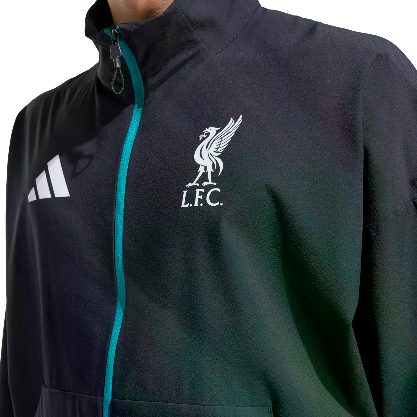 Close-up of a dark Adidas jacket featuring a teal zipper and the white Liverpool F.C. crest on the chest.