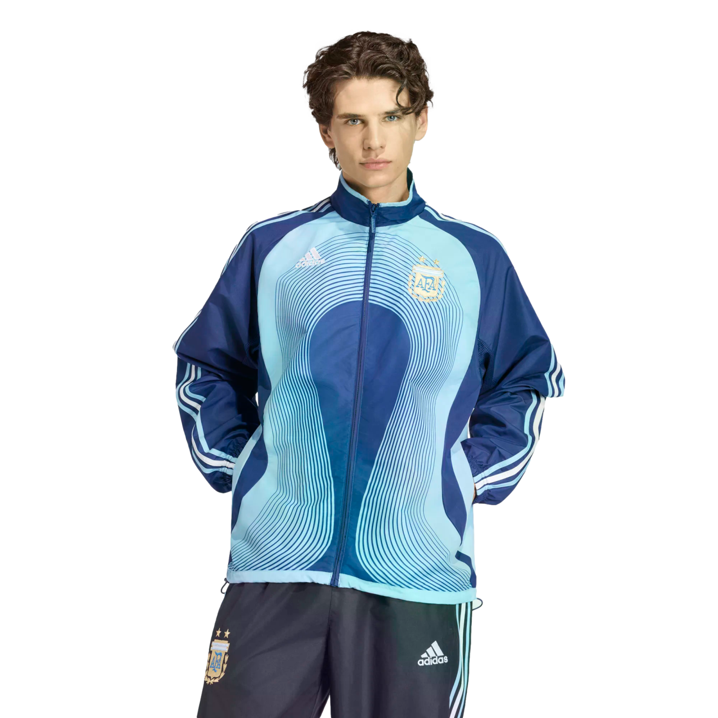 A man wearing a light and dark blue Argentina national team track jacket and matching pants by Adidas, standing against a solid black background.