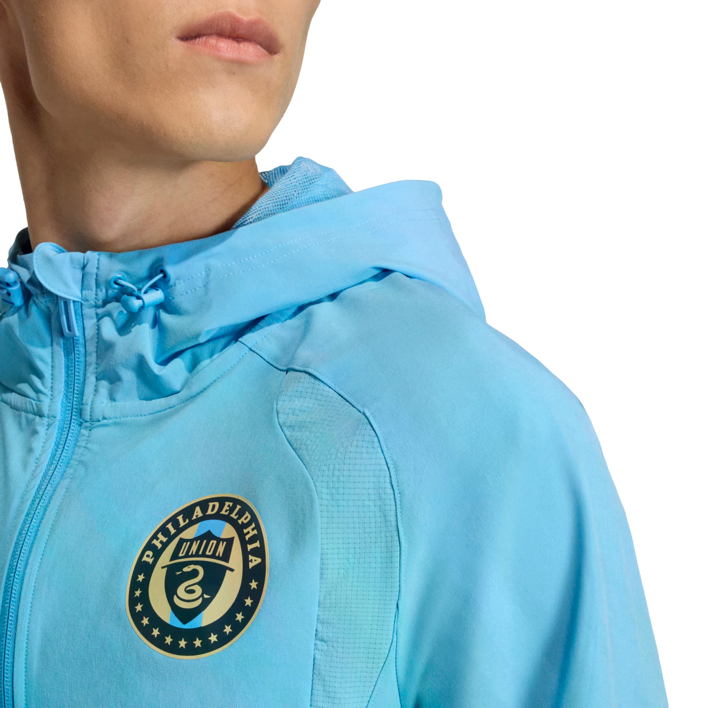 A person wears a light blue Philadelphia Union hooded jacket featuring the team's circular crest on the chest.