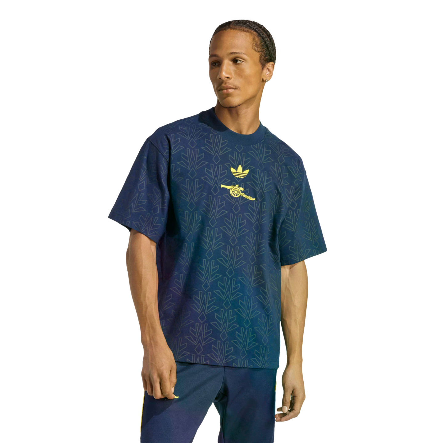 A man modeling a navy blue Adidas x Arsenal t-shirt with a geometric pattern and yellow logos, paired with navy track pants against a black background.
